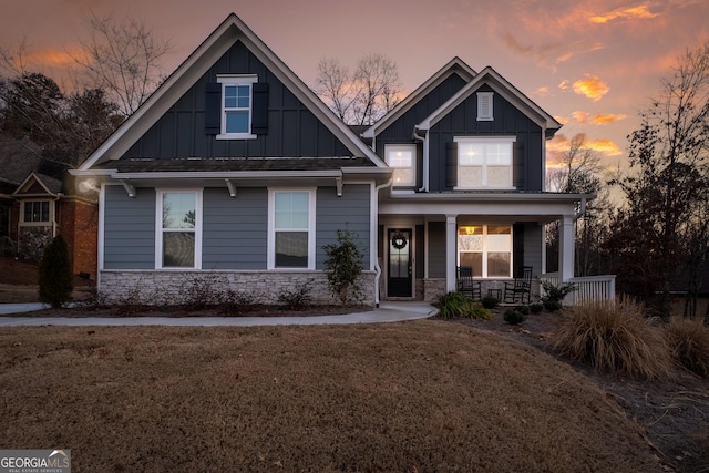 craftsman-style home featuring covered porch, board and batten siding, a front lawn, and stone siding