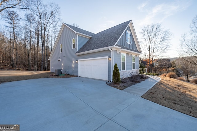 view of side of property featuring central air condition unit, roof with shingles, stone siding, and driveway