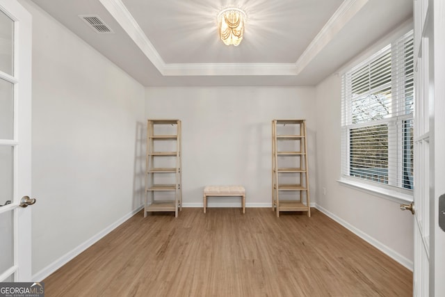 interior space featuring light wood finished floors, ornamental molding, visible vents, and a raised ceiling