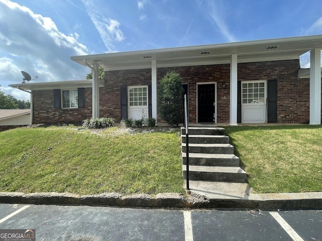 view of front of home with covered porch, brick siding, a front lawn, and uncovered parking