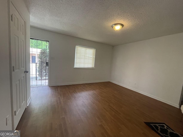 empty room featuring a textured ceiling, visible vents, baseboards, and dark wood-style floors