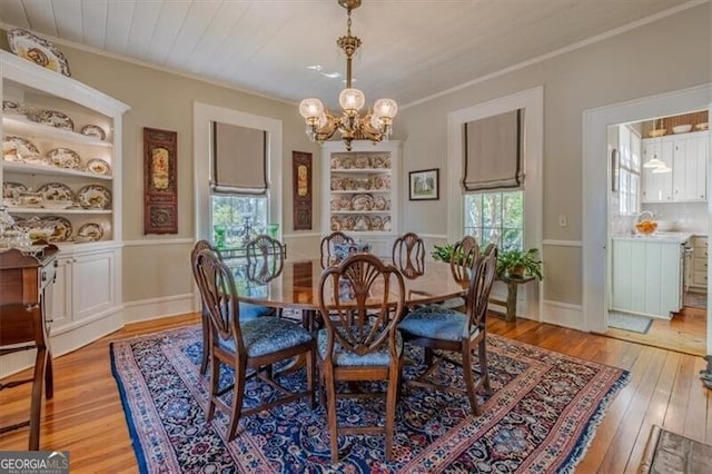dining room featuring built in shelves, light wood finished floors, ornamental molding, and an inviting chandelier