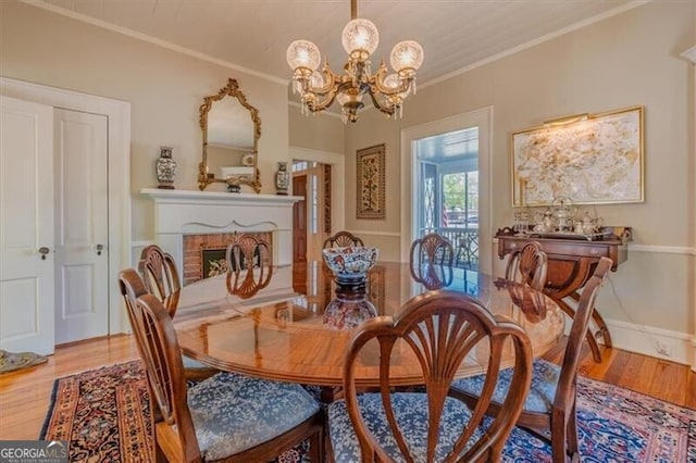 dining area with ornamental molding, a fireplace, a chandelier, and light wood-style floors