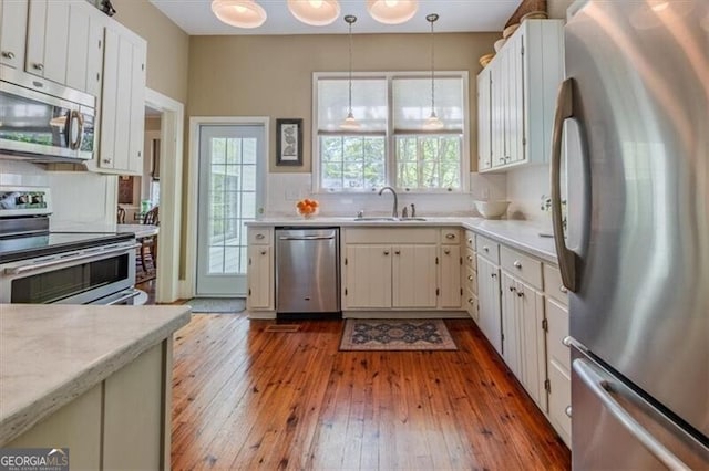 kitchen with stainless steel appliances, decorative light fixtures, a sink, hardwood / wood-style floors, and light countertops