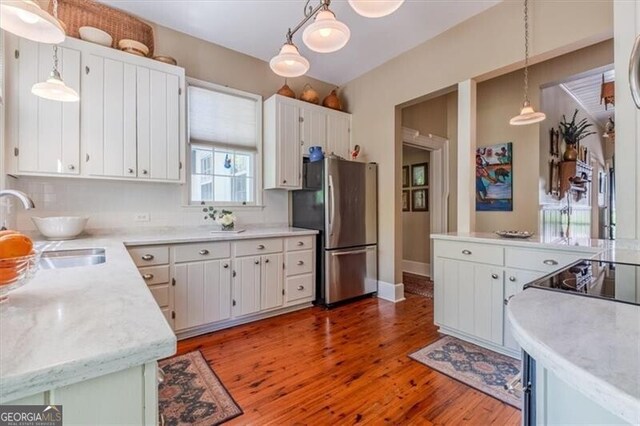 kitchen featuring wood finished floors, a sink, freestanding refrigerator, white cabinets, and light countertops
