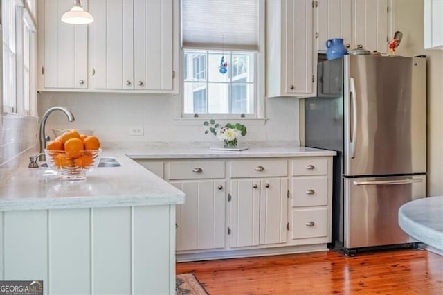 kitchen featuring freestanding refrigerator, white cabinetry, light wood-type flooring, and backsplash