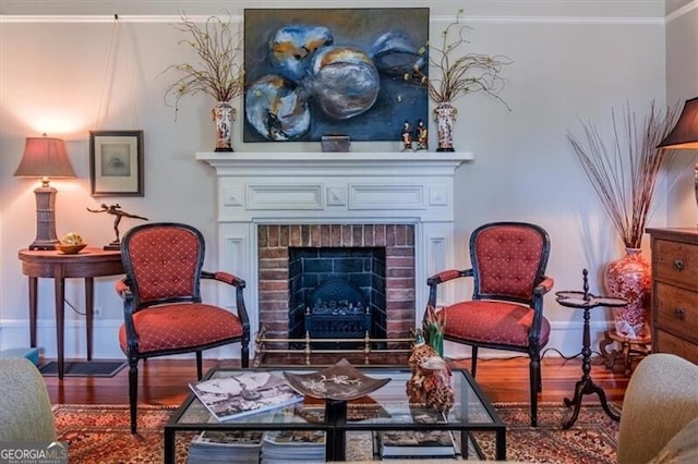 living area with a fireplace, ornamental molding, baseboards, and wood finished floors
