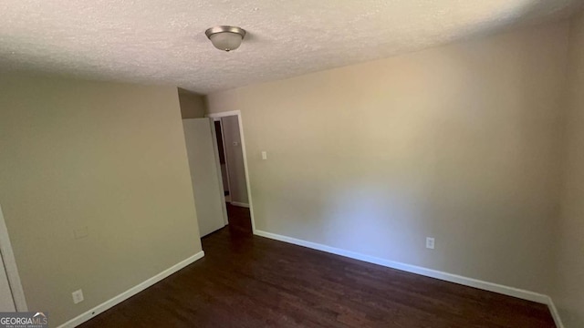 empty room with a textured ceiling, dark wood-type flooring, and baseboards