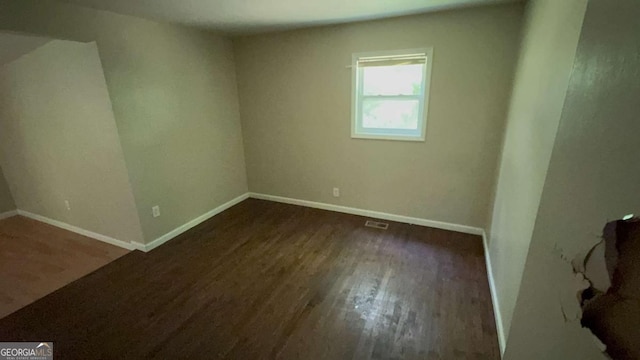 empty room featuring baseboards, dark wood finished floors, and visible vents