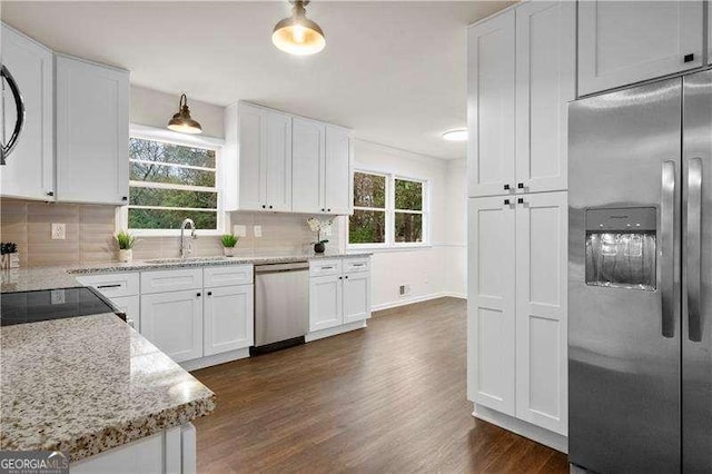 kitchen featuring light stone countertops, dark wood finished floors, a sink, stainless steel appliances, and white cabinets