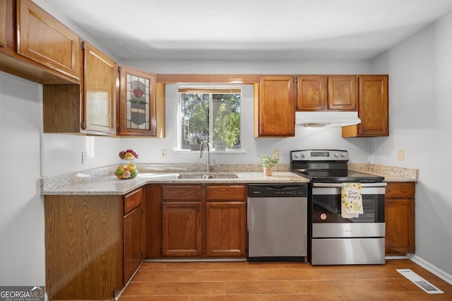 kitchen with a sink, stainless steel appliances, brown cabinets, visible vents, and under cabinet range hood