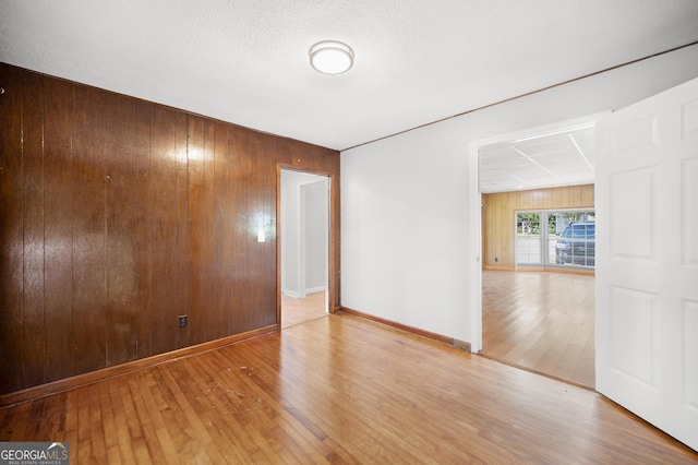 empty room with wooden walls, wood-type flooring, and baseboards