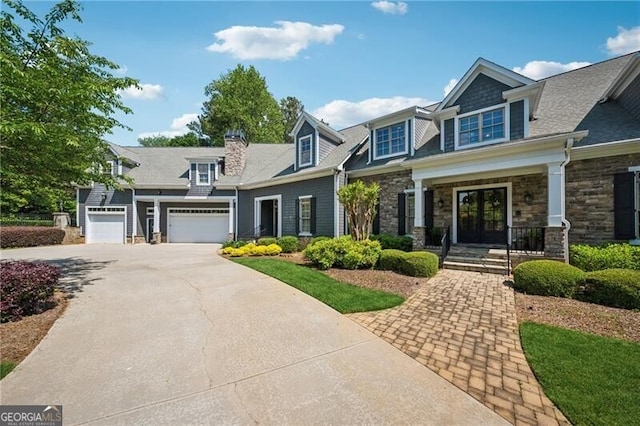 view of front of home with concrete driveway, stone siding, french doors, and covered porch