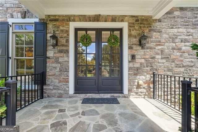 doorway to property featuring stone siding, a porch, and french doors