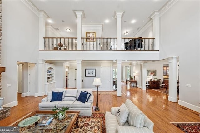 living room featuring wood finished floors, decorative columns, a towering ceiling, crown molding, and baseboards