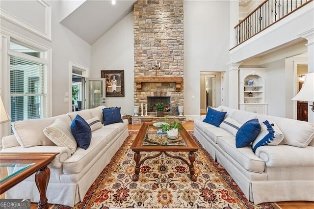 living area featuring a stone fireplace, high vaulted ceiling, ornate columns, and wood finished floors