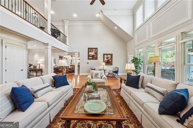 living room featuring ornamental molding, ceiling fan, decorative columns, a towering ceiling, and wood finished floors