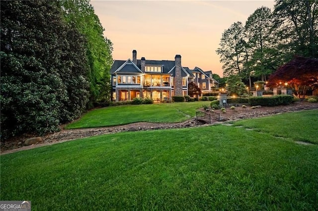 rear view of property featuring a chimney and a lawn