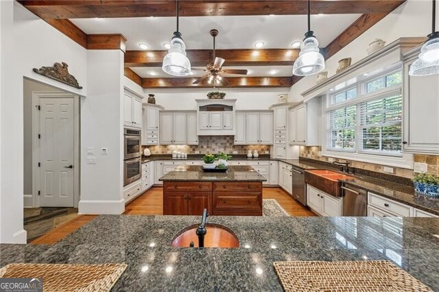 kitchen featuring beam ceiling, stainless steel appliances, decorative backsplash, and dark stone countertops