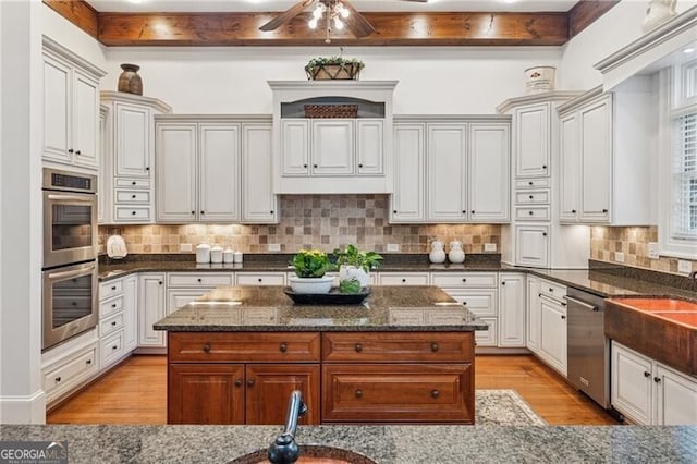 kitchen with a center island, dark stone countertops, stainless steel appliances, light wood-type flooring, and tasteful backsplash