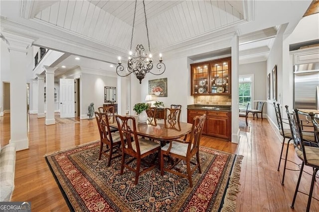 dining area with ornamental molding, ornate columns, light wood finished floors, a notable chandelier, and baseboards