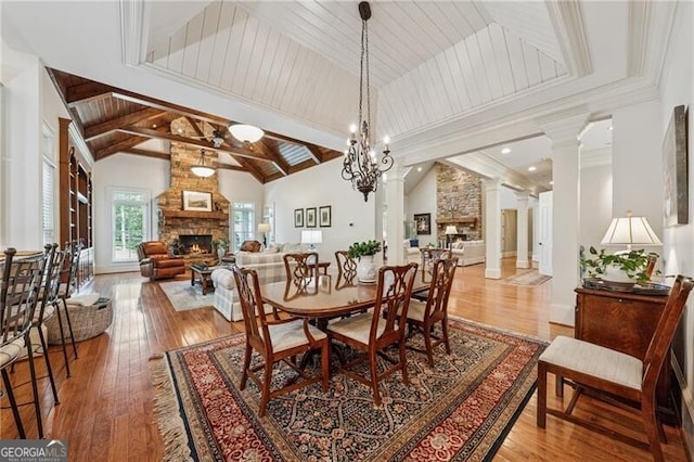 dining space with a stone fireplace, lofted ceiling with beams, decorative columns, and hardwood / wood-style flooring