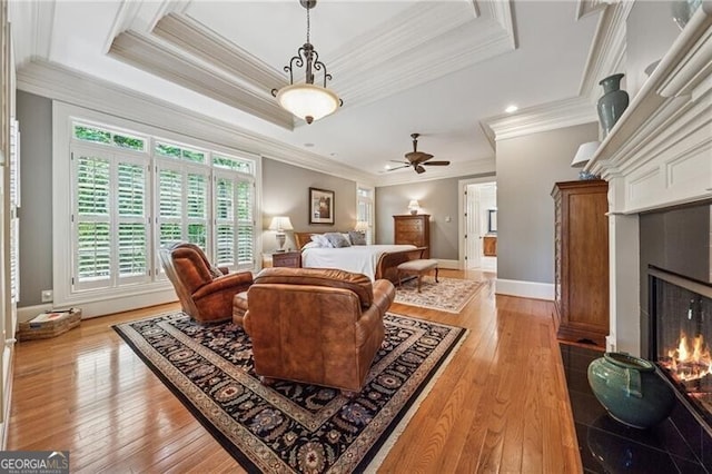 living room featuring baseboards, light wood finished floors, crown molding, a lit fireplace, and a raised ceiling