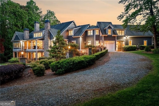 shingle-style home with gravel driveway, a chimney, and a garage
