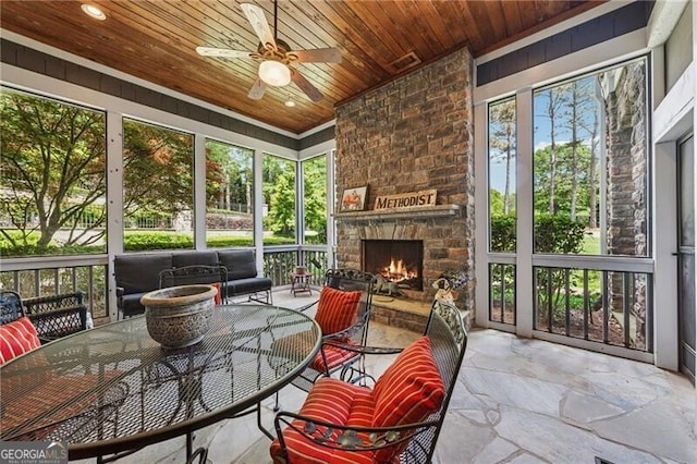 sunroom with a fireplace, outdoor dining space, and a ceiling fan