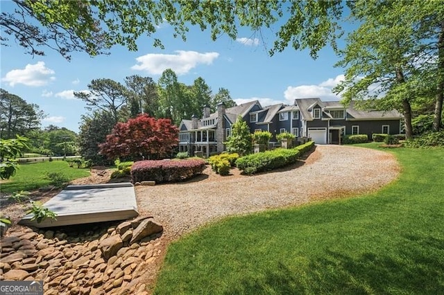 view of home's community featuring an attached garage, a lawn, and gravel driveway