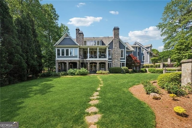 back of property with a lawn, stone siding, and a balcony