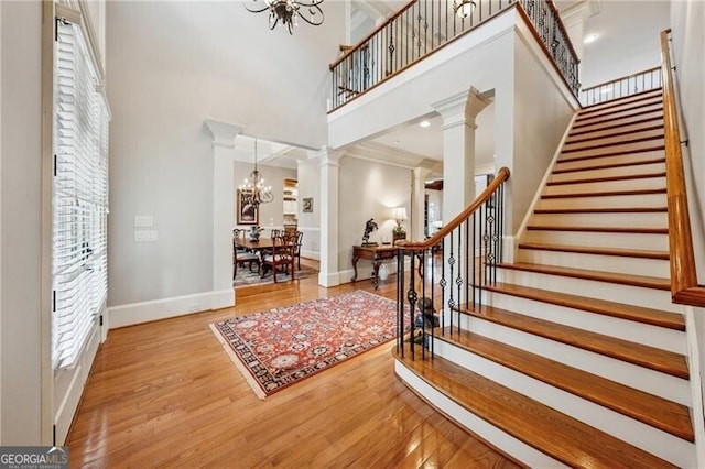entrance foyer featuring decorative columns, a chandelier, wood finished floors, stairway, and a high ceiling