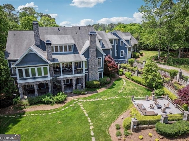 back of house featuring a chimney, stone siding, fence private yard, and a lawn