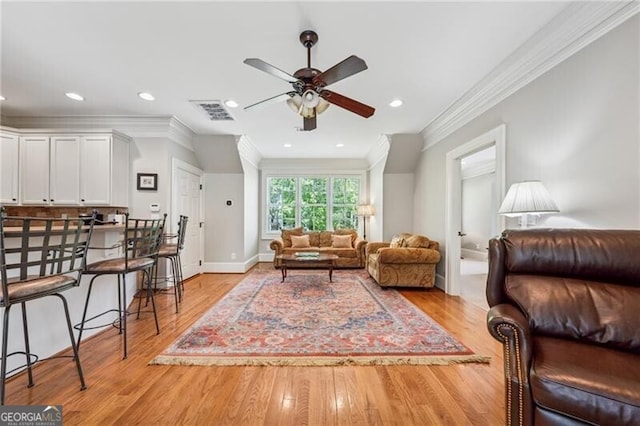 living room with light wood-type flooring, visible vents, a ceiling fan, and ornamental molding