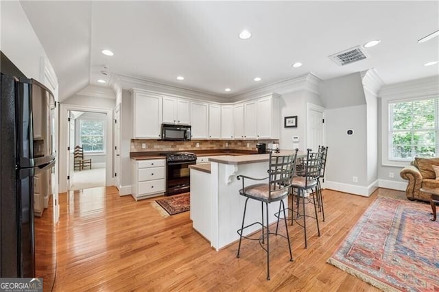 kitchen with a breakfast bar, a healthy amount of sunlight, black appliances, and visible vents