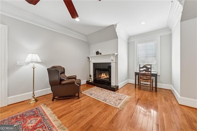 living area with a tile fireplace, wood finished floors, a ceiling fan, crown molding, and baseboards