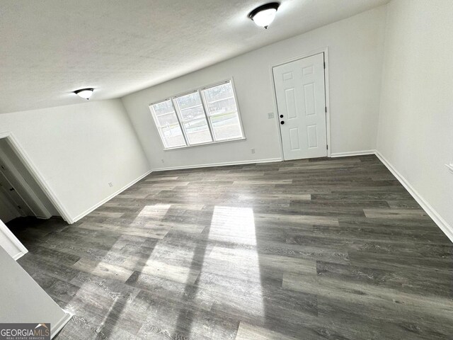 unfurnished living room with dark wood-style flooring, baseboards, and a textured ceiling
