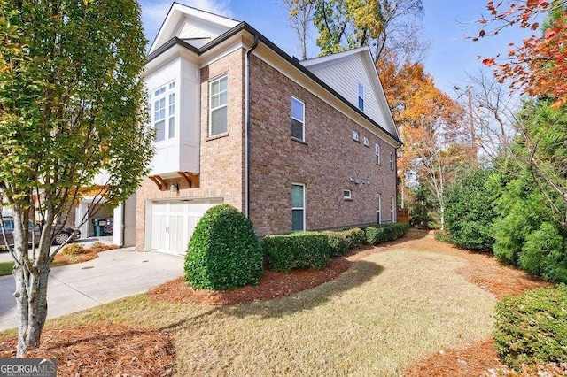 view of home's exterior with an attached garage, brick siding, driveway, and a lawn