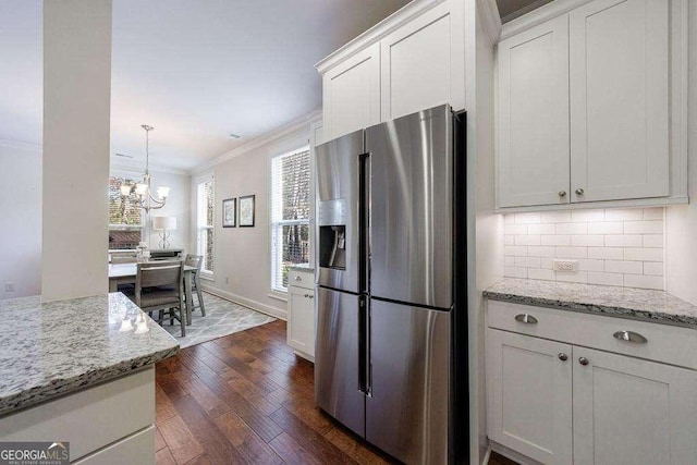kitchen with a notable chandelier, dark wood finished floors, stainless steel fridge, crown molding, and decorative backsplash