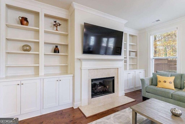 living room featuring ornamental molding, visible vents, built in shelves, dark wood finished floors, and a premium fireplace