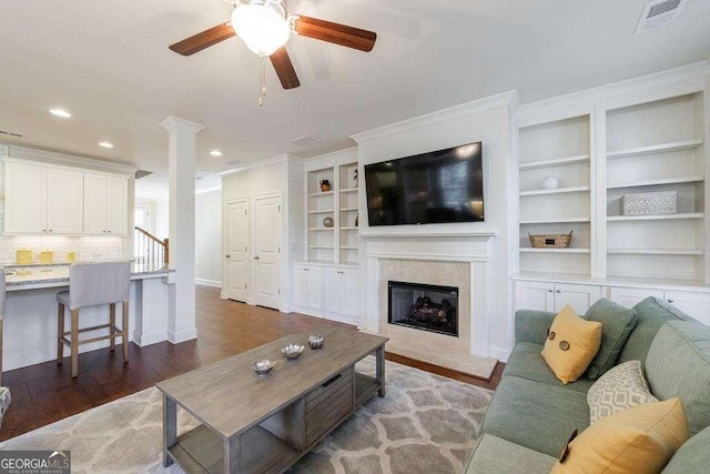 living area with wood finished floors, a ceiling fan, a fireplace, decorative columns, and visible vents