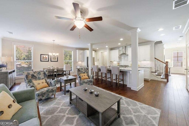 living room featuring dark wood-style flooring, ornamental molding, visible vents, and ceiling fan with notable chandelier