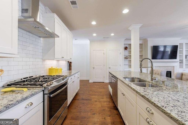 kitchen featuring a sink, wall chimney exhaust hood, stainless steel appliances, open floor plan, and crown molding