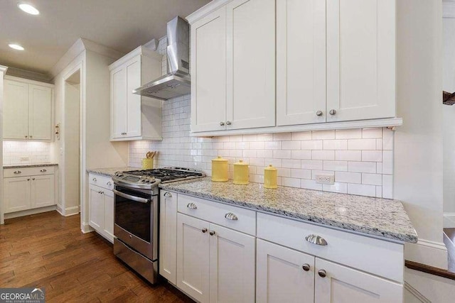 kitchen featuring white cabinets, wall chimney exhaust hood, stainless steel gas range oven, and decorative backsplash