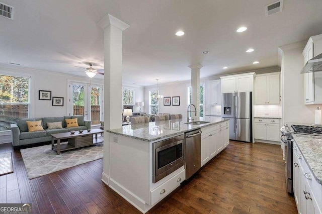 kitchen with a sink, decorative columns, open floor plan, crown molding, and appliances with stainless steel finishes