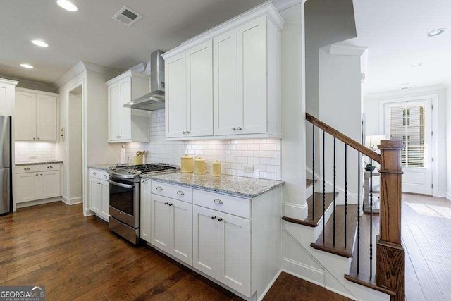 kitchen with dark wood-style flooring, stainless steel appliances, visible vents, and wall chimney exhaust hood