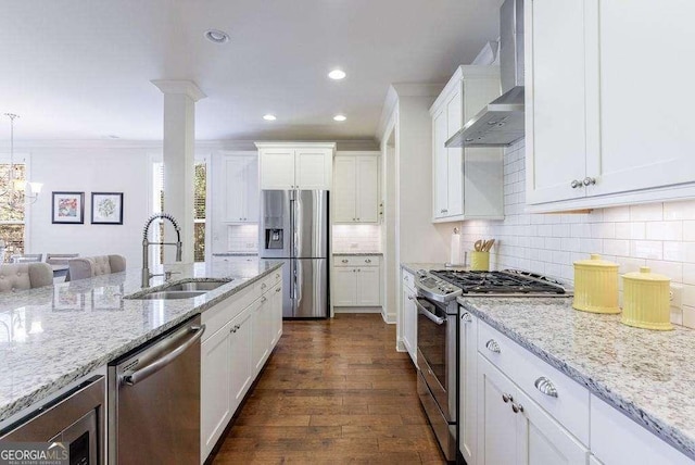kitchen with recessed lighting, a sink, wall chimney range hood, white cabinets, and appliances with stainless steel finishes