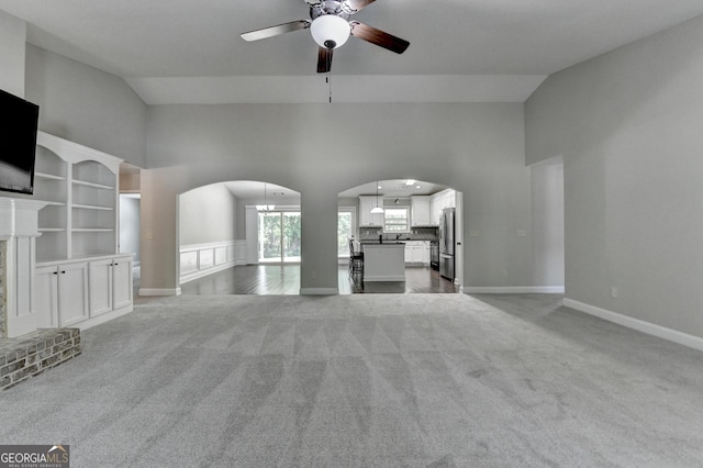 unfurnished living room featuring high vaulted ceiling, baseboards, ceiling fan, arched walkways, and light carpet