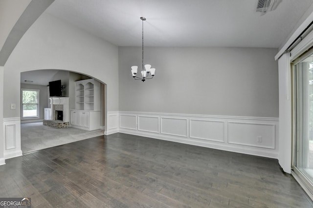 unfurnished dining area with dark wood finished floors, wainscoting, visible vents, a brick fireplace, and arched walkways