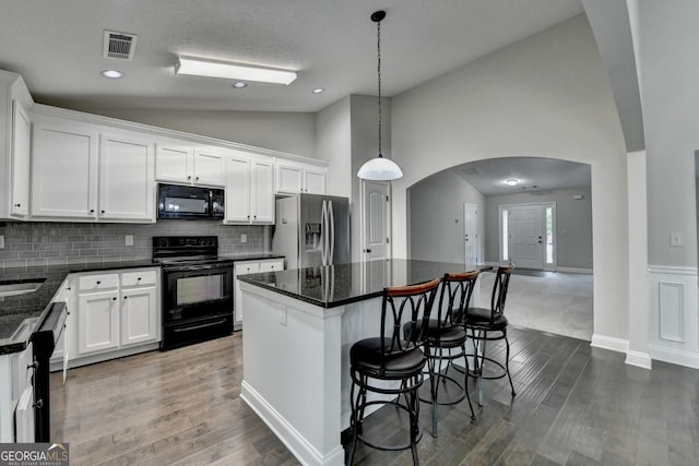 kitchen with a center island, visible vents, vaulted ceiling, arched walkways, and black appliances